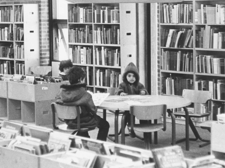 Tre små børn sidder ved et bord på biblioteket. Sort/hvid